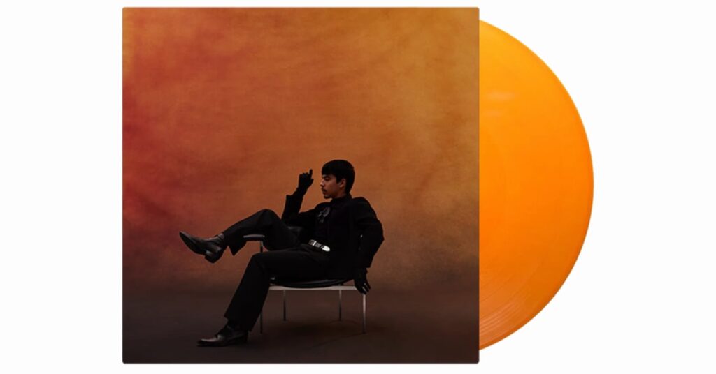 Ivan Cornejo's "Mirada" album cover. He is seen sitting on a chair against a warm, orange-brown background. An orange vinyl record is partially visible beside the cover.