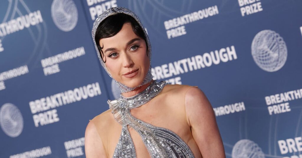 Katy Perry at the Breakthrough Prize event, wearing a sparkling silver gown with a matching headpiece, posing on the red carpet.