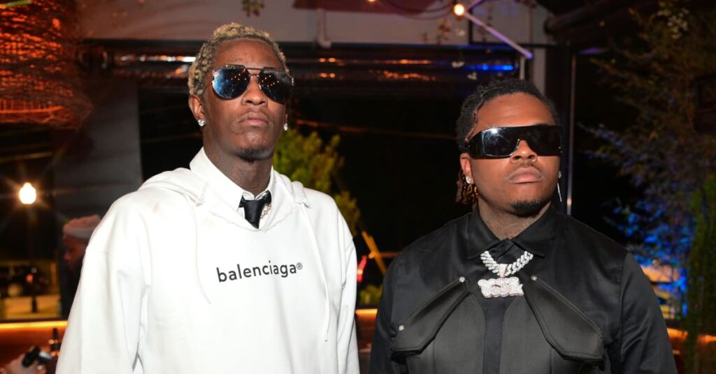 Young Thug and Gunna posing together; Young Thug in a white Balenciaga hoodie, Gunna in black with sunglasses and jewelry.