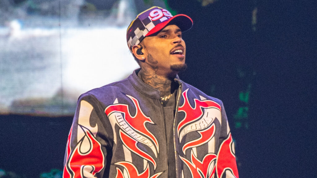 Chris Brown performing on stage, wearing a jacket with flame designs and a cap with the number 98.