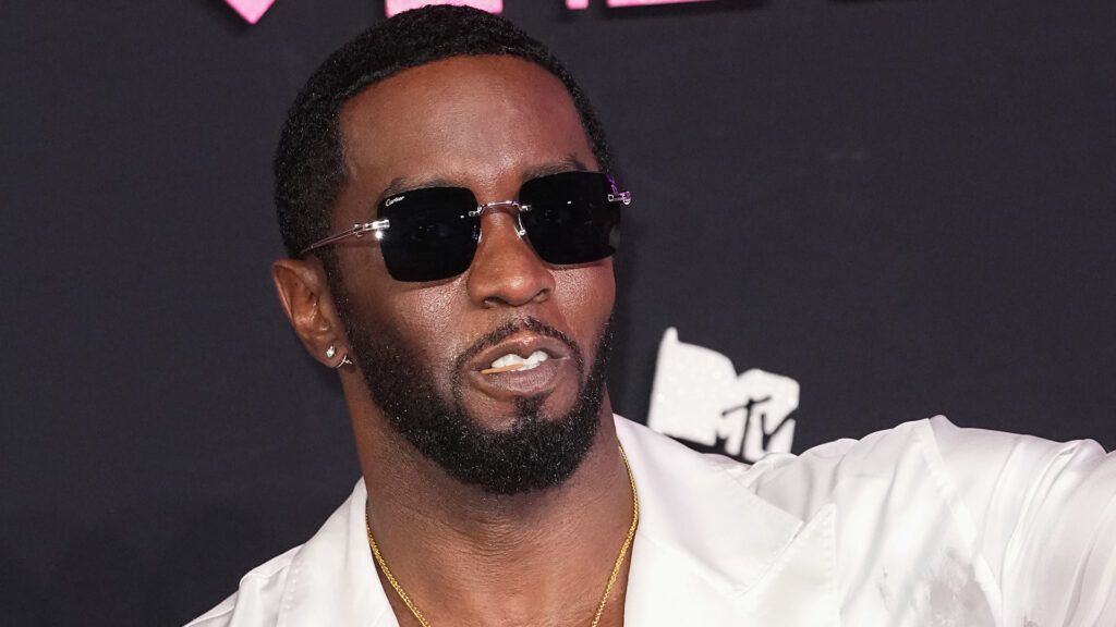 Diddy wearing sunglasses and a white outfit at an event with a black background featuring the MTV logo.
