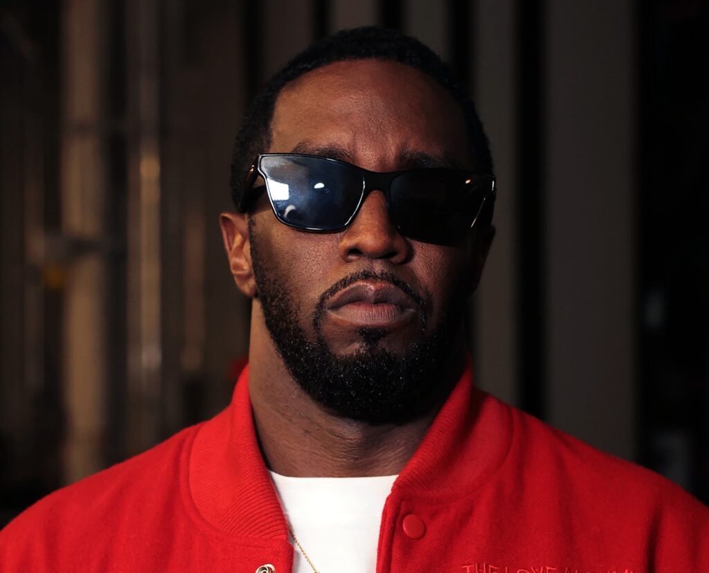 Diddy wearing sunglasses and a red jacket, looking directly at the camera with a serious expression.
