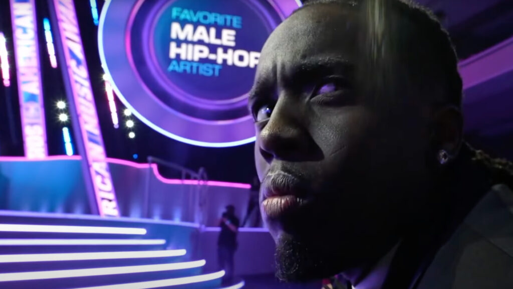 Kai Cenat on Eminem Winning at American Music Awards: ‘Le… Kai Cenat in a black tuxedo smiling, and Eminem performing on stage with a microphone, wearing a dark jacket and cap.