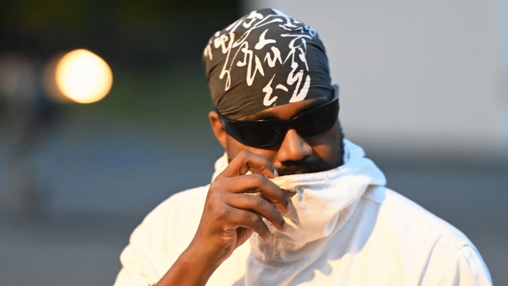 A person wearing a patterned headscarf, sunglasses, and a white jacket, partially covering their face.