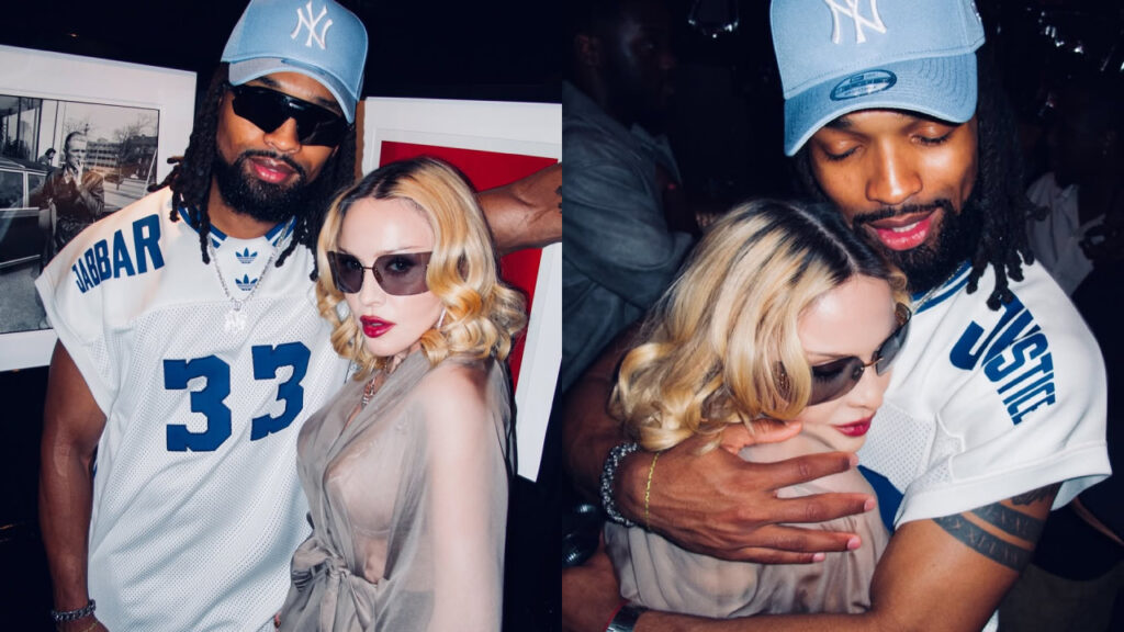 Madonna with blonde hair and sunglasses poses with boyfriend Akeem Morris wearing a blue cap and a sports jersey. They appear to be at an event.