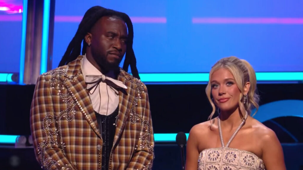 Two people on stage, Shaboozey with long dreadlocks and a plaid suit, Megan Moroney with blonde hair in a ponytail, wearing a strapless dress.