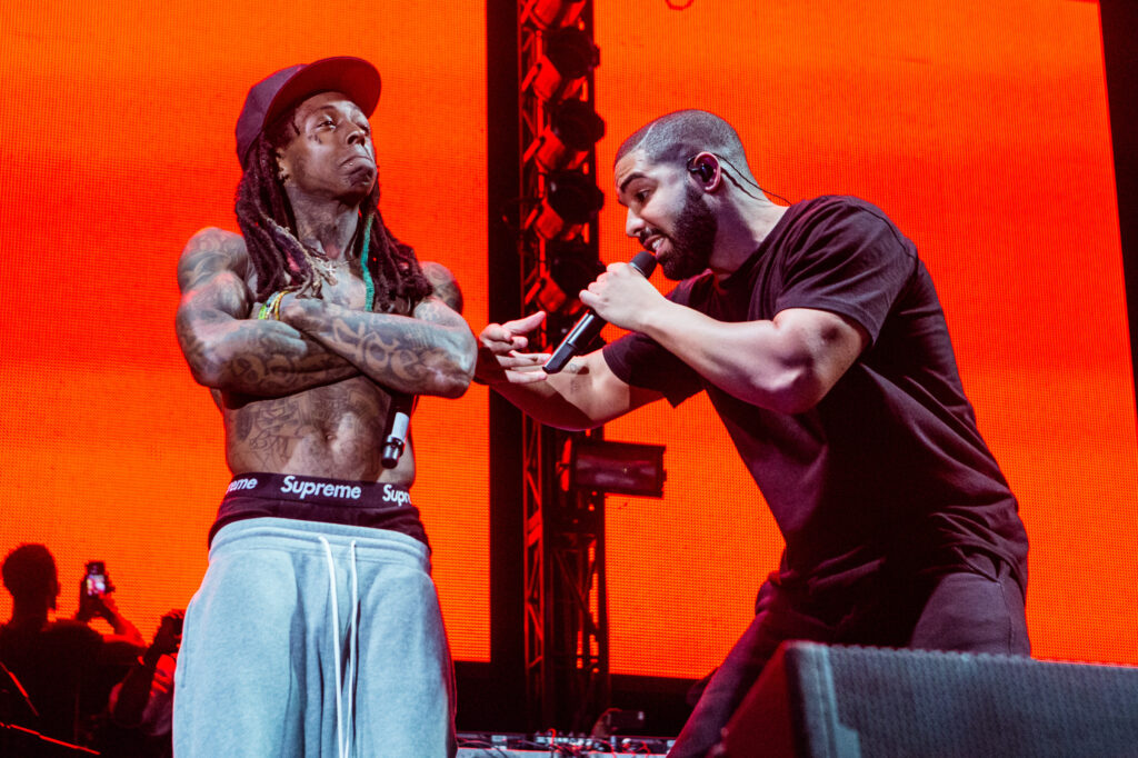 Lil Wayne with no shirt and Drake with a black shirt holding a mic. Bot are performing.