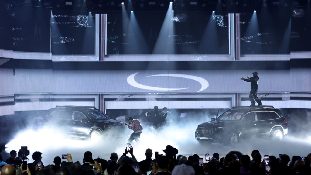 A Playboi Carti stage performance with two SUVs, fog effects, dancers, and an audience capturing the scene.