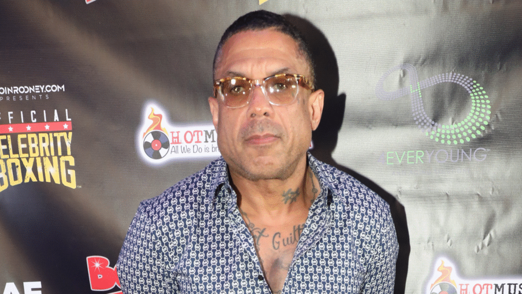 A man in glasses and a patterned shirt stands in front of a backdrop featuring "Celebrity Boxing" logos.