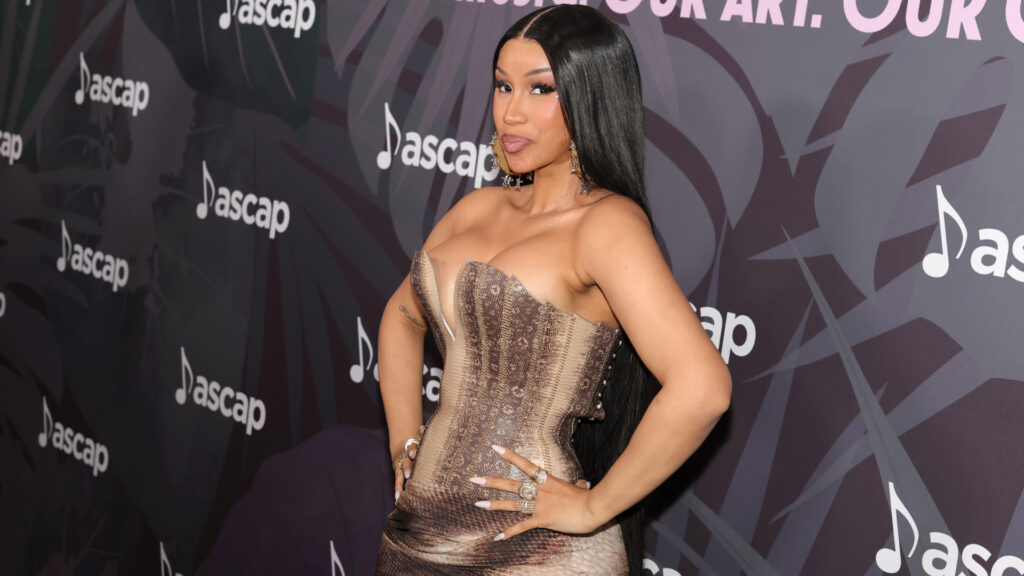 Cardi B poses confidently in a strapless dress at an ASCAP event, with a patterned backdrop featuring the ASCAP logo.