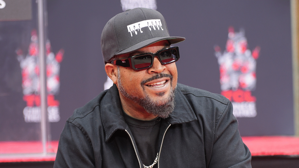 Ice Cube, wearing sunglasses and a black cap, smiles at an event with a TCL Chinese Theatre backdrop.