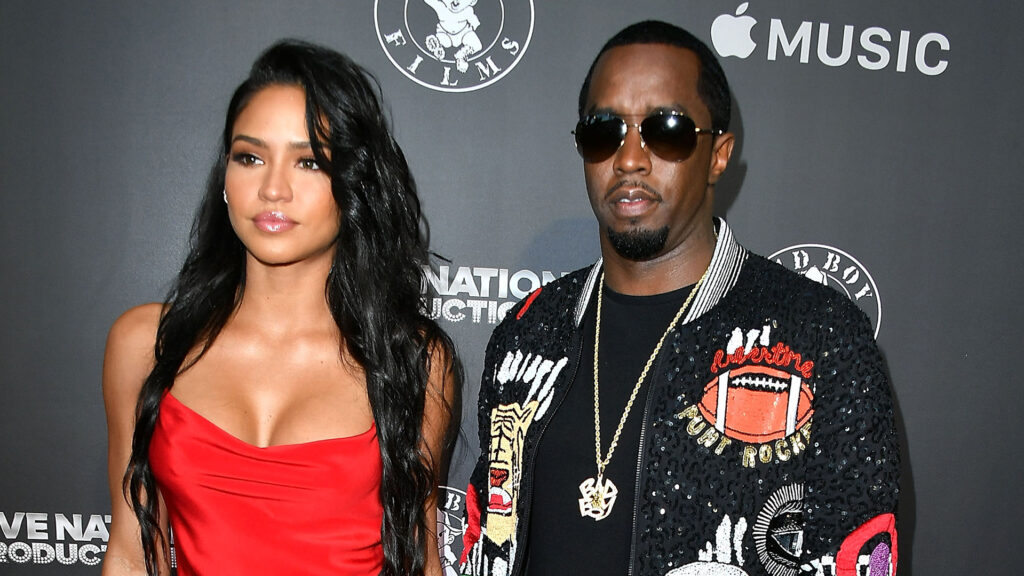 Cassie in a red dress and Sean "Diddy" Combs in sunglasses and a patterned jacket pose at an event.
