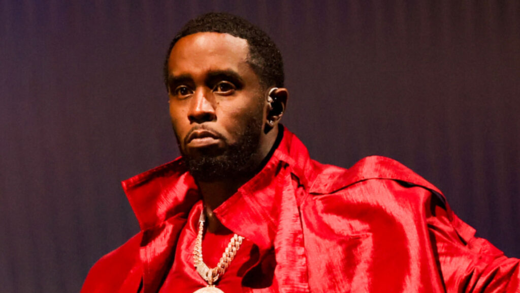 Sean "Diddy" Combs wearing a red outfit and chain necklace, looking serious against a dark background.
