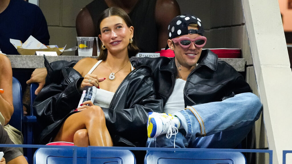 Justin Bieber Says He’s a ‘Dad That’s Not to Be F*cked Wi… Hailey Bieber and Justin Bieber sitting together at an event, both wearing black jackets. Hailey has a white top, Justin wears a polka dot hat.
