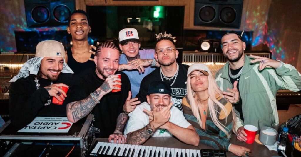 A group of people in a recording studio, including J Balvin and Karol G, smiling and posing with musical equipment.