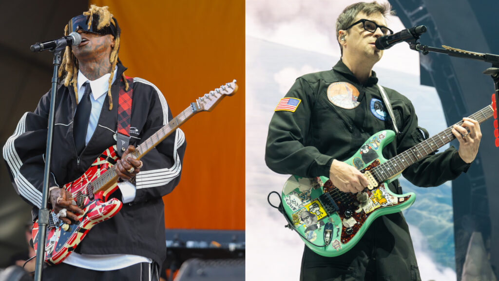 Lil Wayne and Rivers Cuomo performing on stage, each playing guitars. Lil Wayne wears a black outfit with a red guitar, and Rivers Cuomo wears a black jumpsuit with patches and a sticker-covered guitar.