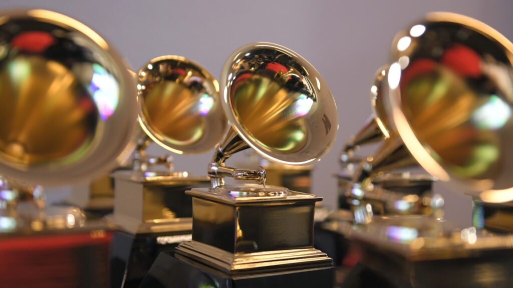 A close-up of multiple Grammy Awards trophies, featuring gold gramophones on black bases, with a blurred background.