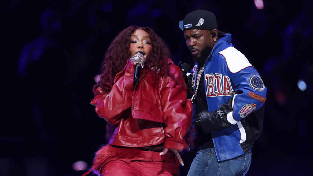 SZA and Kendrick Lamar perform on stage. SZA wears a red outfit, while Kendrick wears a blue and white jacket and a cap.