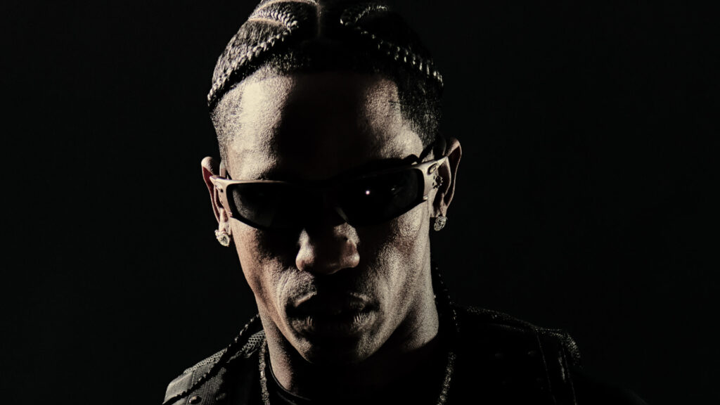 Travis Scott with braided hair and sunglasses, set against a dark background.