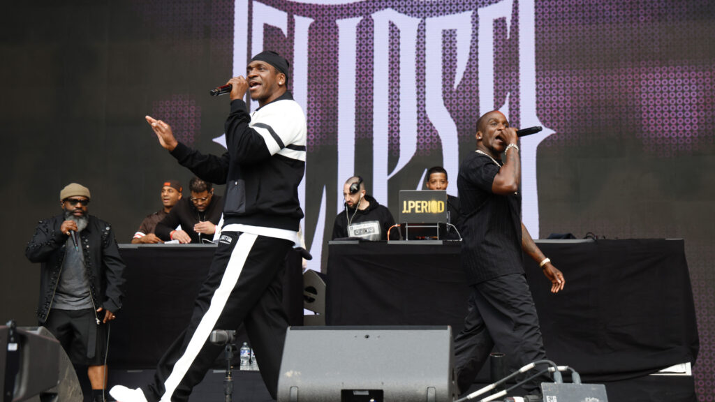 Clipse performing on stage with a DJ in the background, energetically engaging with the audience.