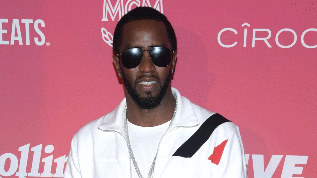 Sean "Diddy" Combs wearing sunglasses and a white jacket, standing in front of a pink background with logos.