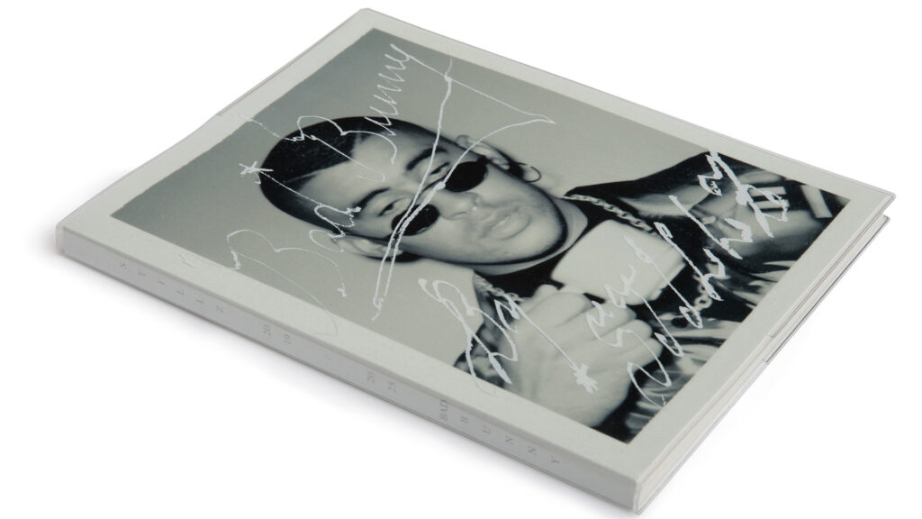 Bad Bunny Subject of Andy Warhol-Inspired Photography Boo… A book featuring a black and white image of Bad Bunny wearing sunglasses, with his autograph on the cover.